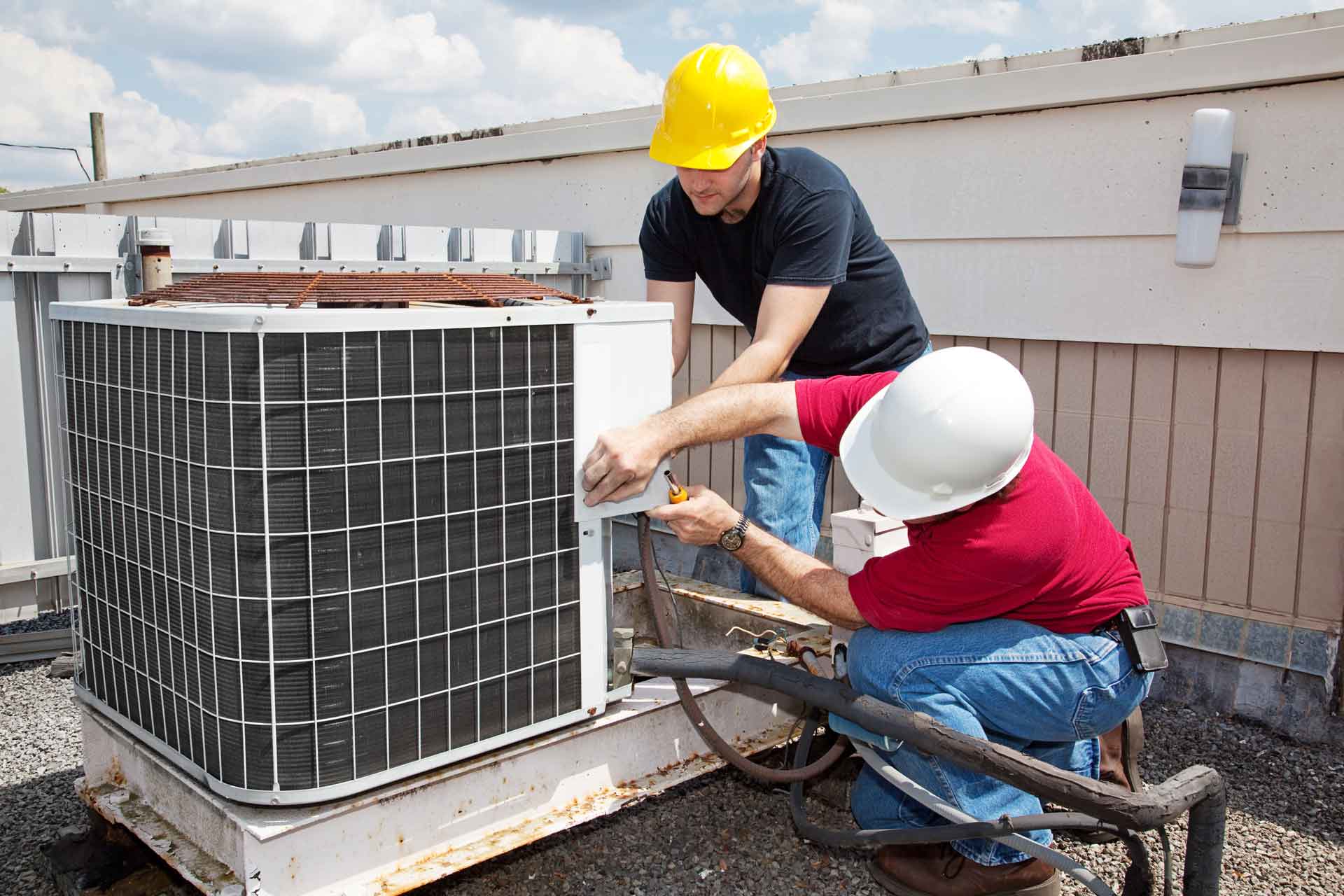 Two HVAC technicians work on an air conditioning unit
