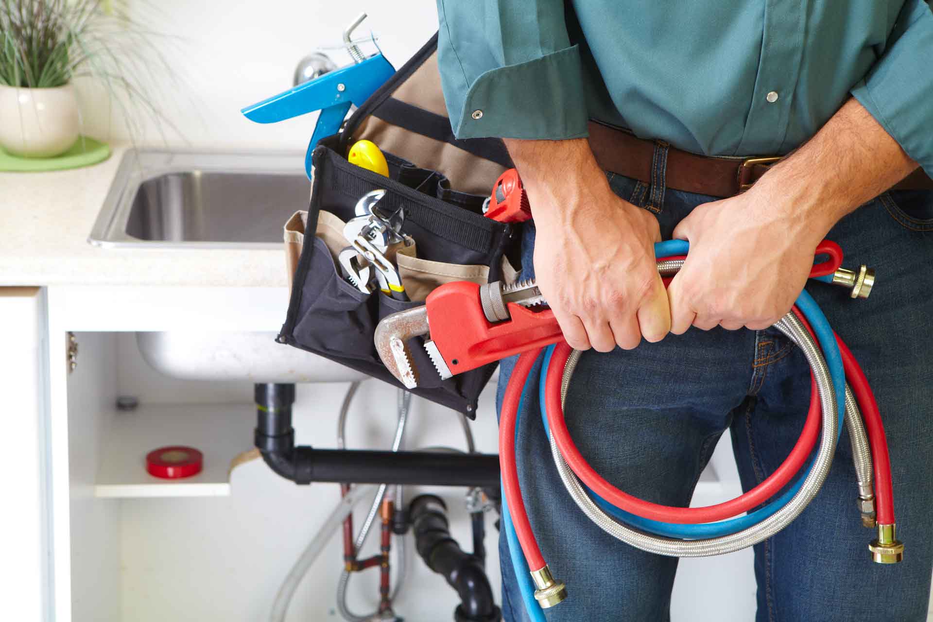 A plumber holding a handful of coiled hoses and a wrench